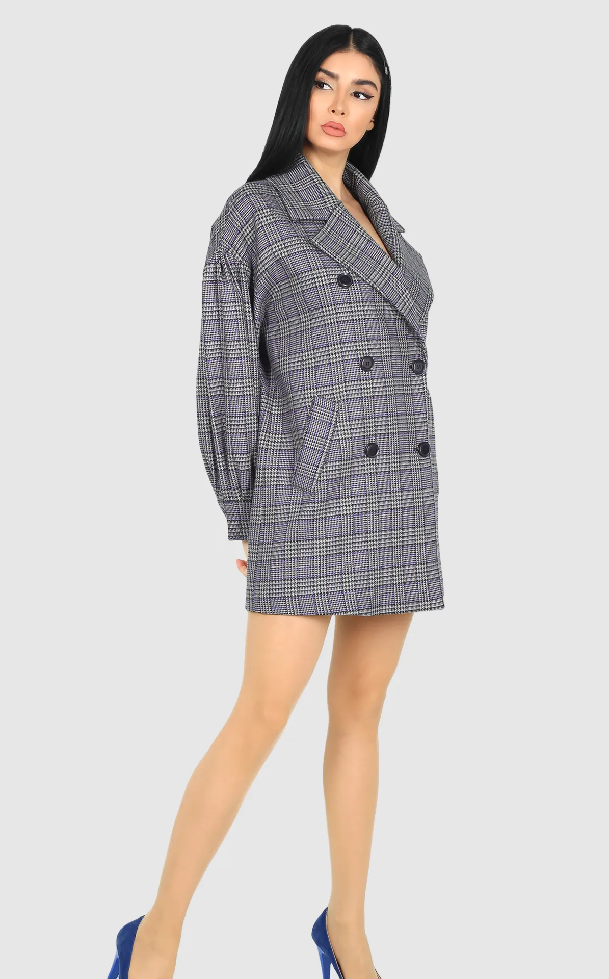A woman in a checked double-breasted coat dress and blue heels.
